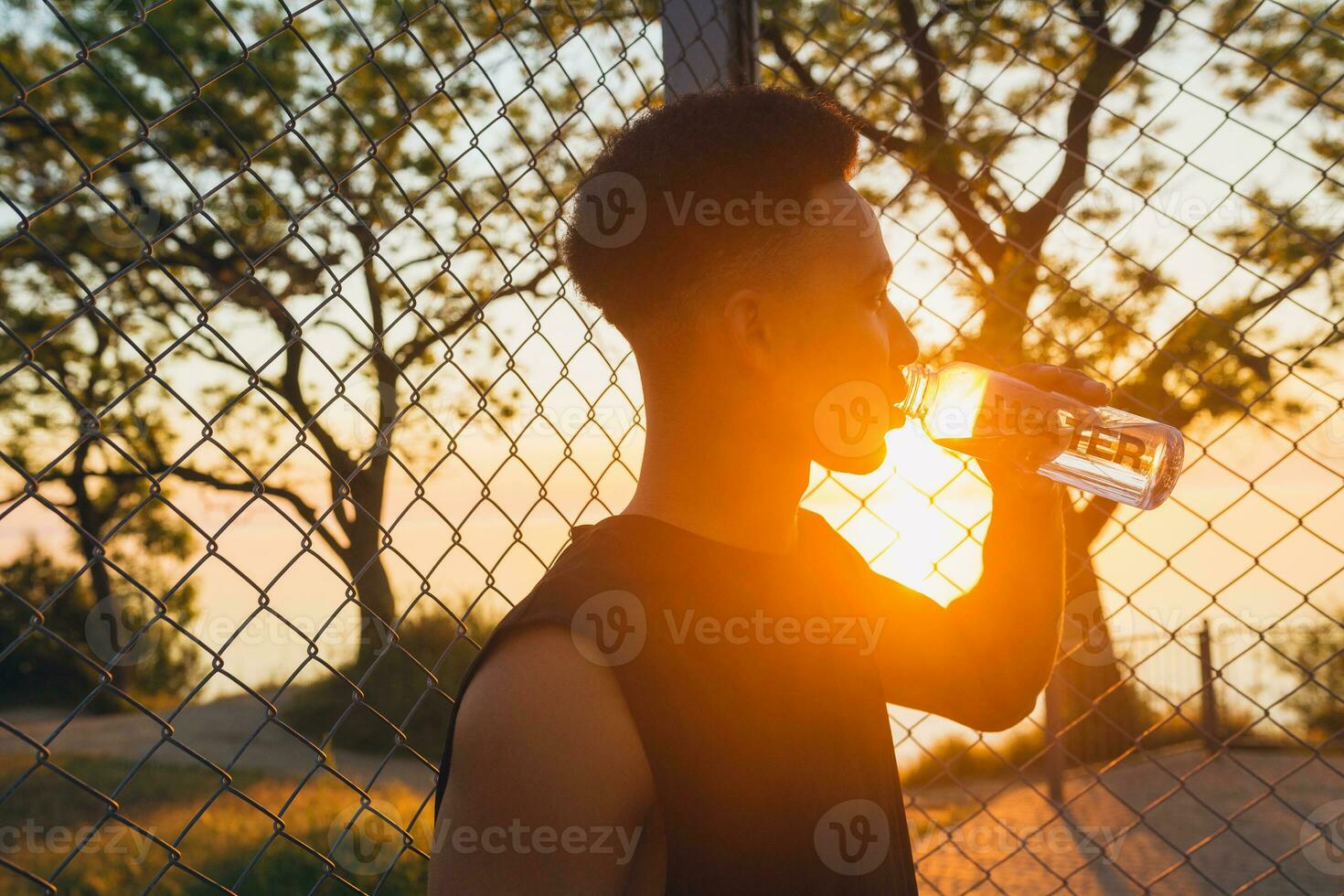 negro hombre haciendo Deportes en mañana, Bebiendo agua en baloncesto Corte en amanecer foto