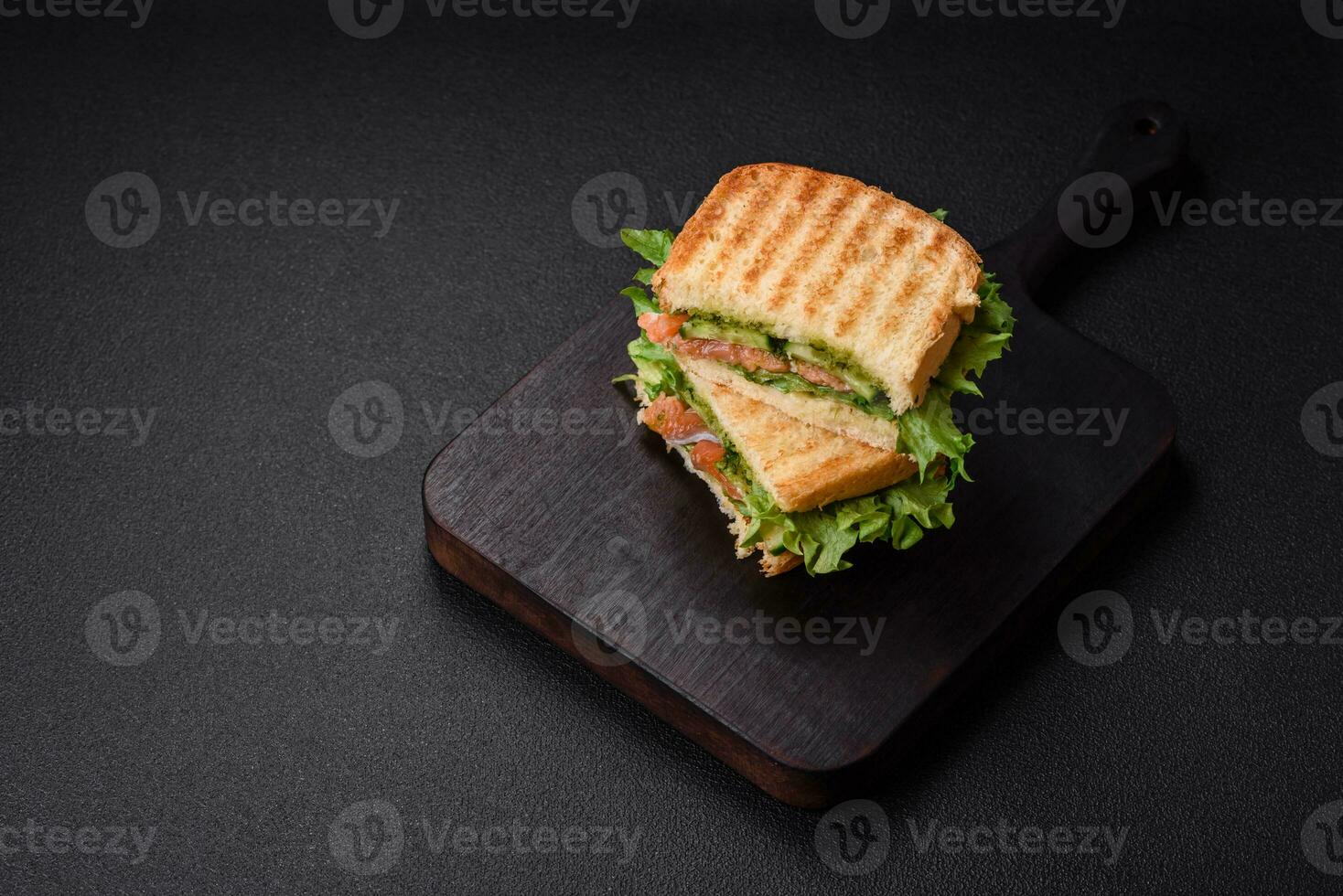 Delicious crispy sandwich with toast, salmon, avocado, tomatoes, salt, spices and herbs photo