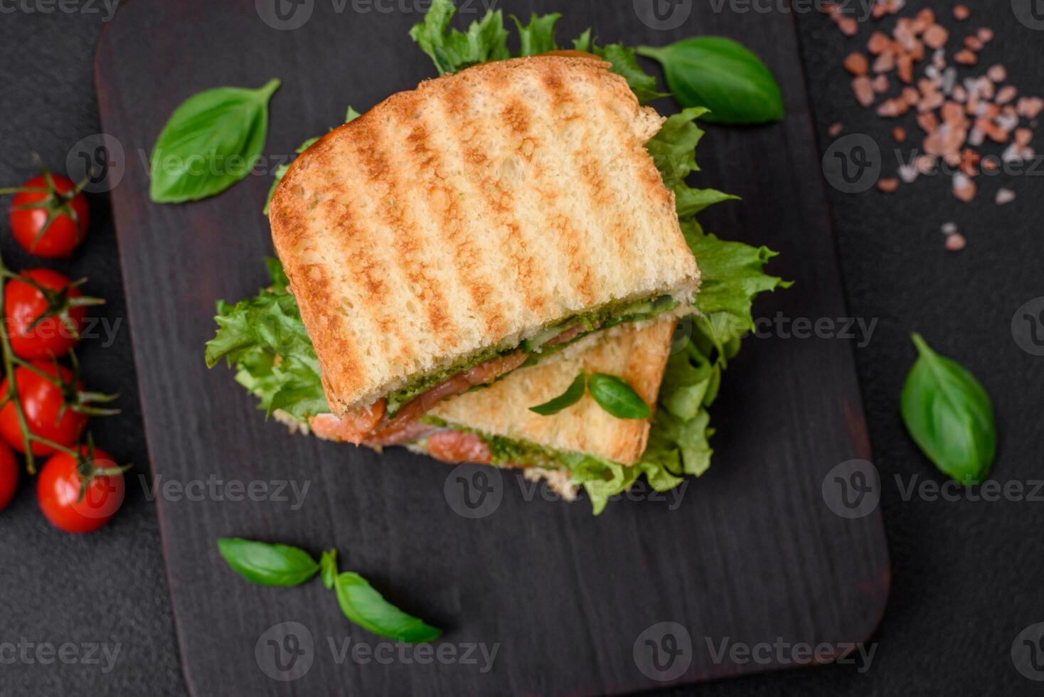 Delicious crispy sandwich with toast, salmon, avocado, tomatoes, salt, spices and herbs photo