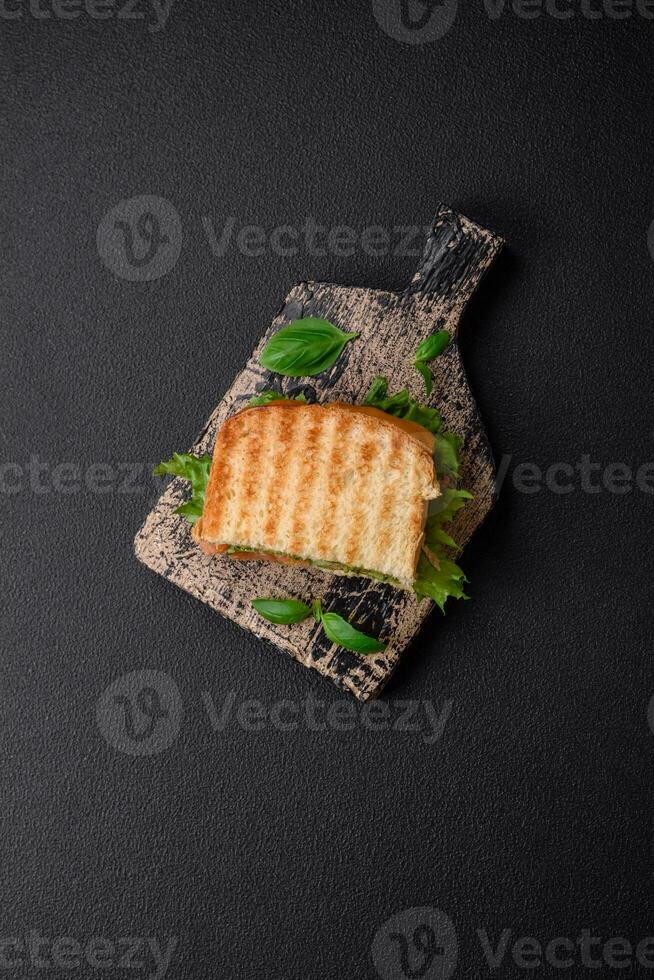 Delicious crispy sandwich with toast, salmon, avocado, tomatoes, salt, spices and herbs photo