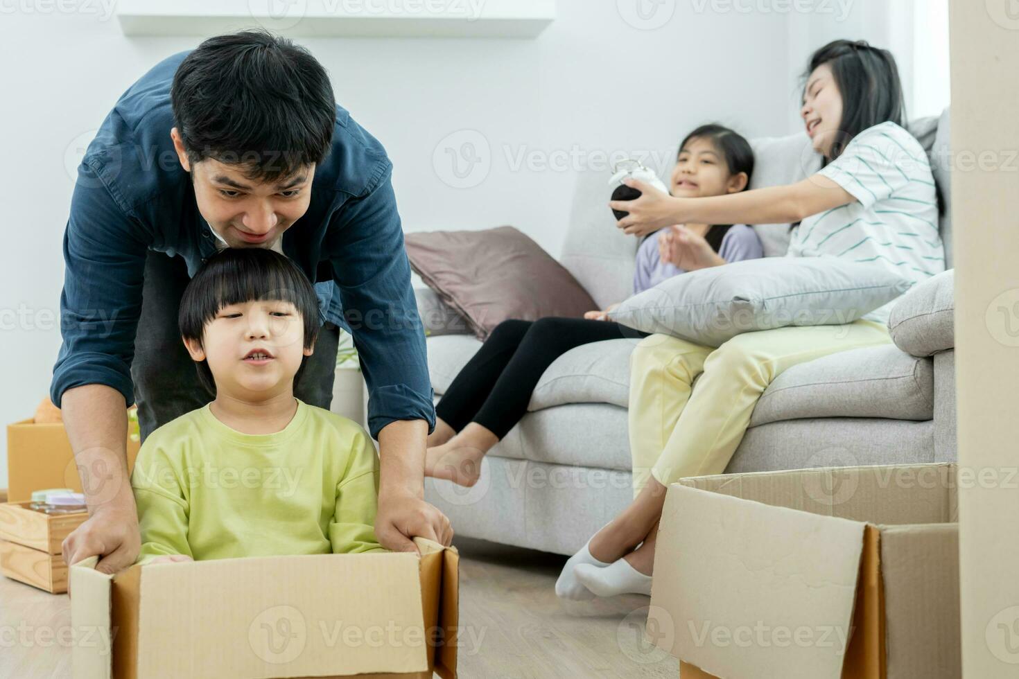 Moviente casa, reubicación familia sonrisa y jugar juntos después moverse a nuevo hogar, dentro el habitación estaba un cartulina caja Contiene personal pertenencias y mueble. moverse en el nuevo departamento, condominio foto