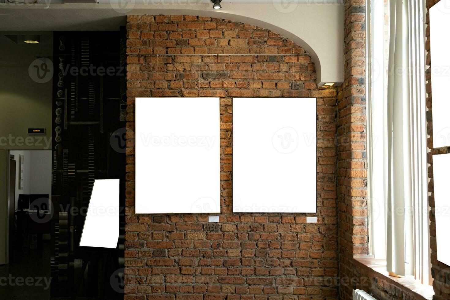 Blank picture frames on brick wall with glowing lamp, mock up photo