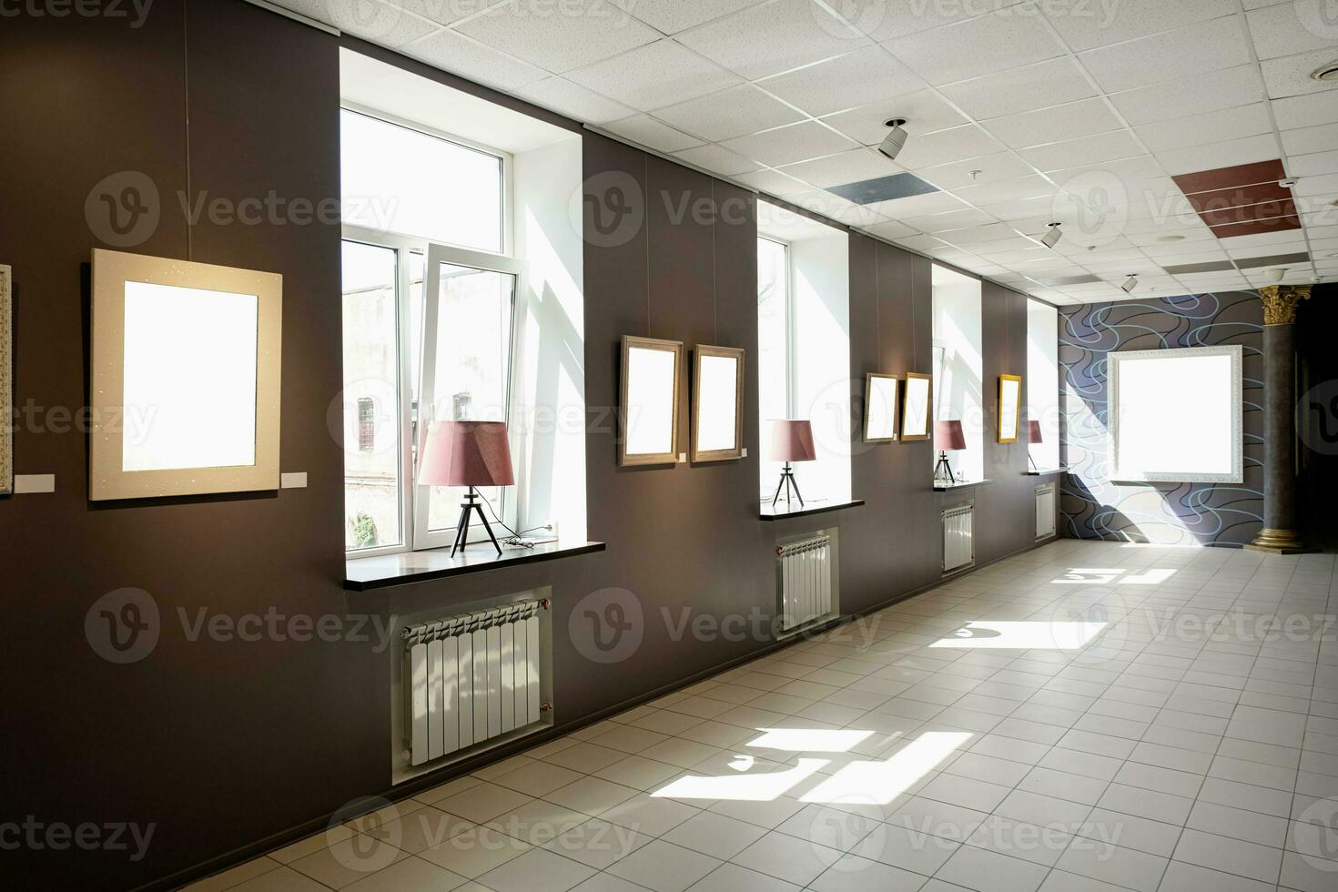 Blank picture frames on brown wall with glowing lamp, mock up photo