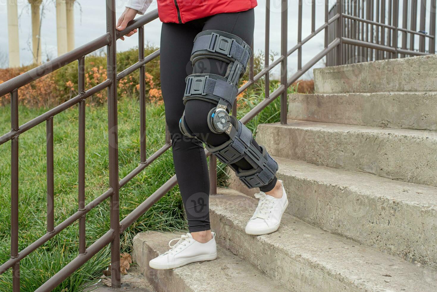 Woman wearing knee brace or orthosis after leg surgery, walking in the park photo