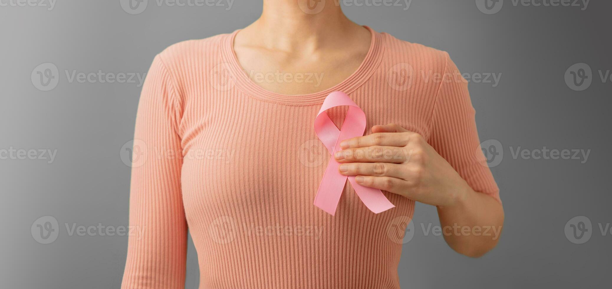 Breast Cancer Awareness Campaign Concept. Women Healthcare. Close up of a Young Female Touching Pink Ribbon on her Thorax photo