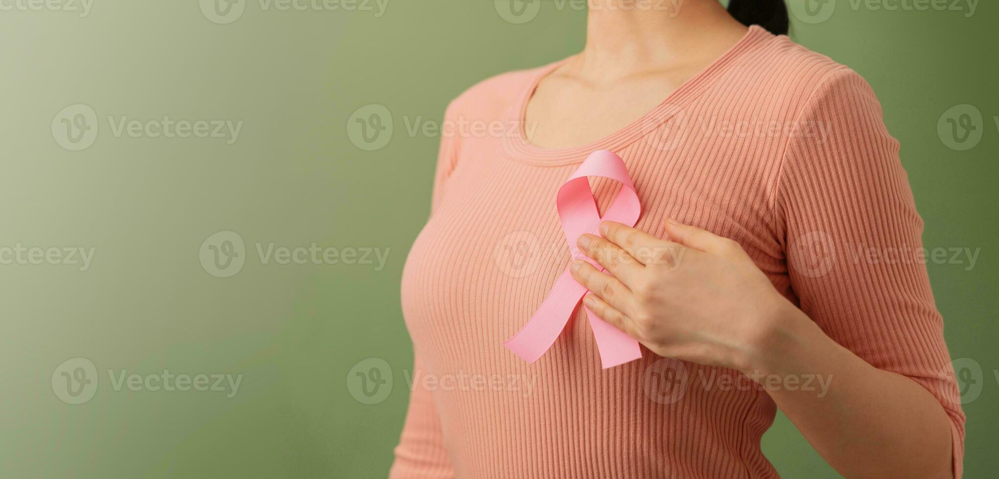 Breast Cancer Awareness Campaign Concept. Women Healthcare. Close up of a Young Female Touching Pink Ribbon on her Thorax photo