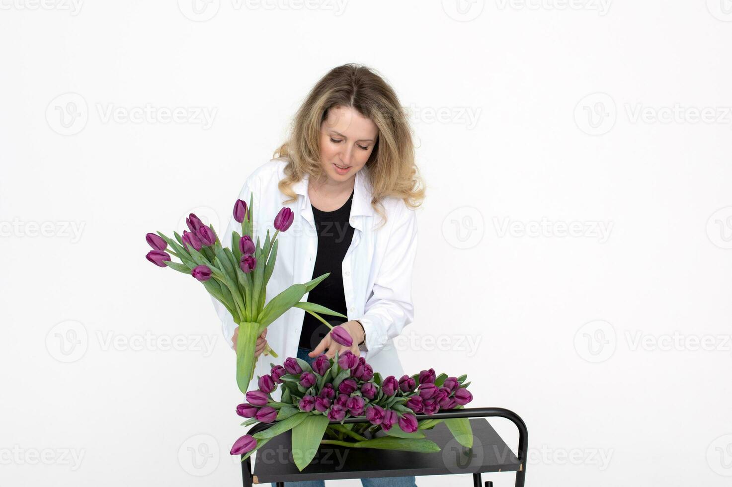 linda niña florista en un camisa recoge un ramo de flores de púrpura tulipanes para un regalo para de la madre día foto