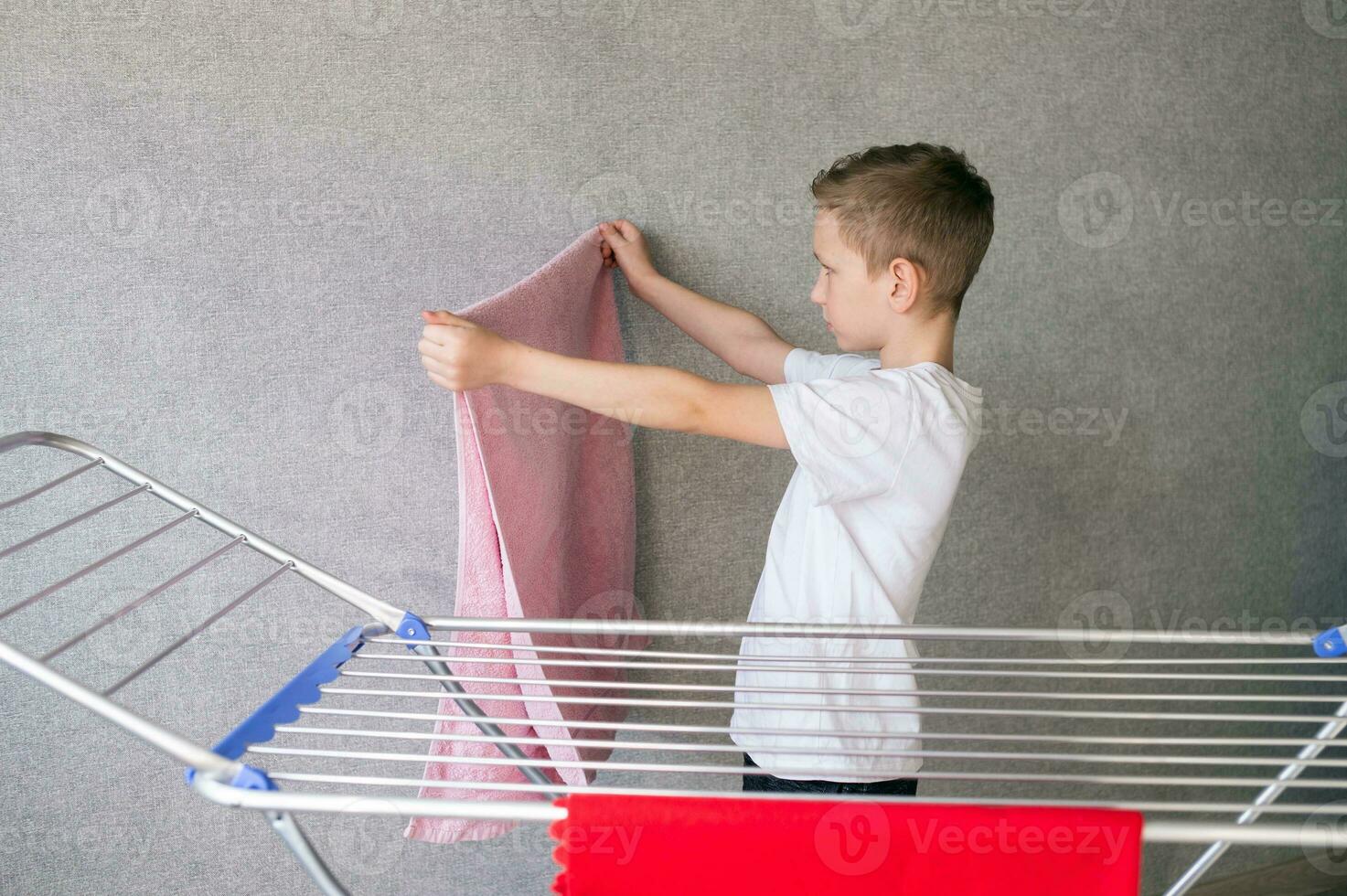 Cute boy doing household chores, hanging wet clothes on the dryer photo
