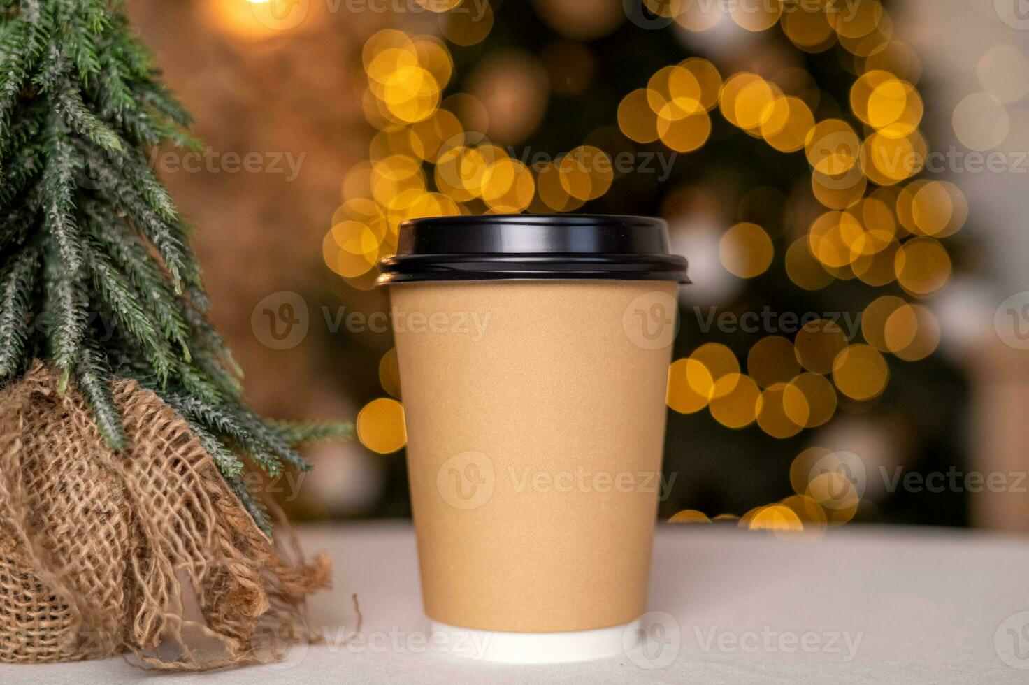 A disposable coffee cup with a lid on the background of a Christmas tree. Place for advertising photo
