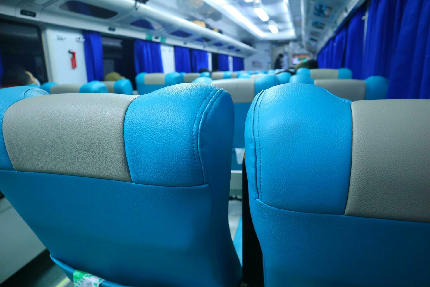 Executive class train interior with blue seats, armrests, luggage racks, monitor screens, air conditioning, and lights that extend on the ceiling photo