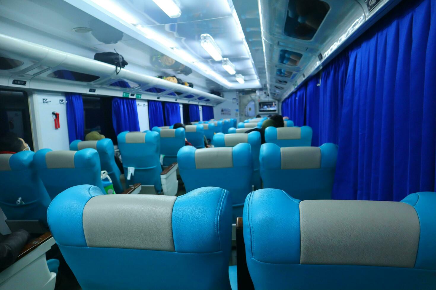 Executive class train interior with blue seats, armrests, luggage racks, monitor screens, air conditioning, and lights that extend on the ceiling photo