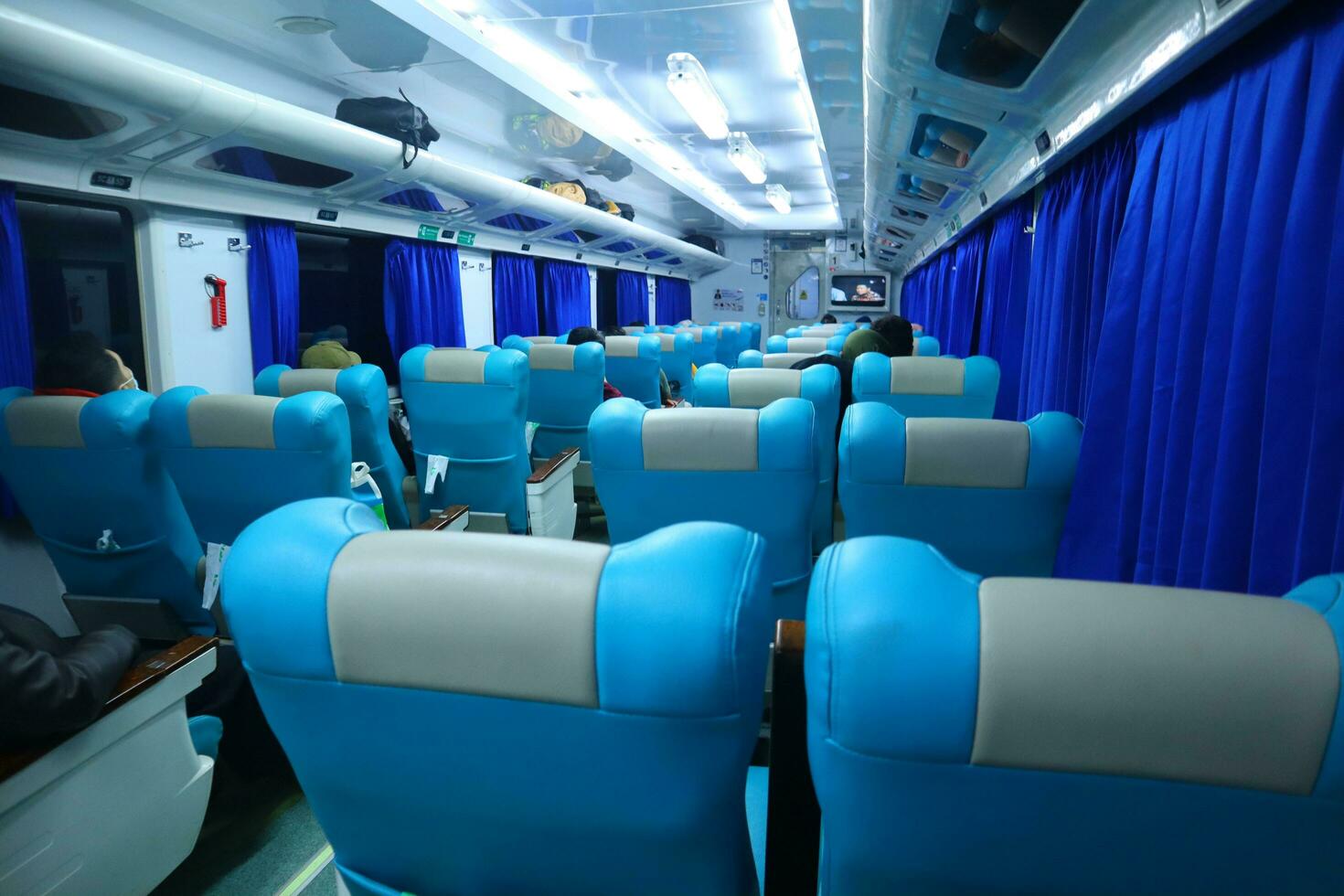 Executive class train interior with blue seats, armrests, luggage racks, monitor screens, air conditioning, and lights that extend on the ceiling photo