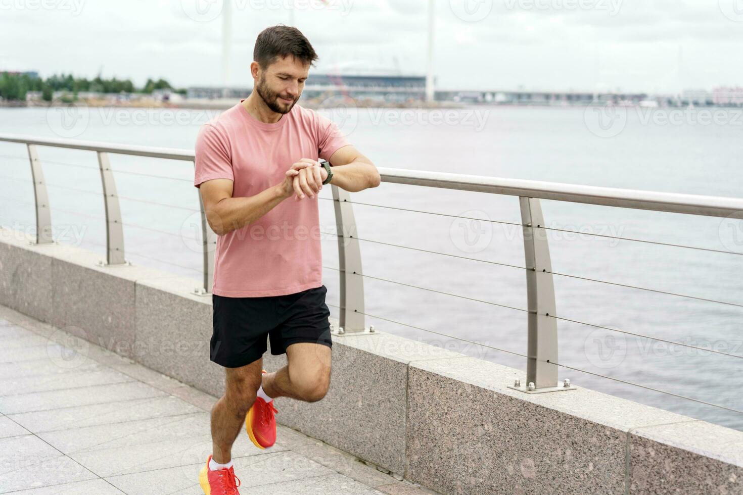 The running coach is a man and trains outdoors. Runner athlete in fitness clothes and running shoes, full-length. Uses a fitness watch for a strong person and sports for health. photo