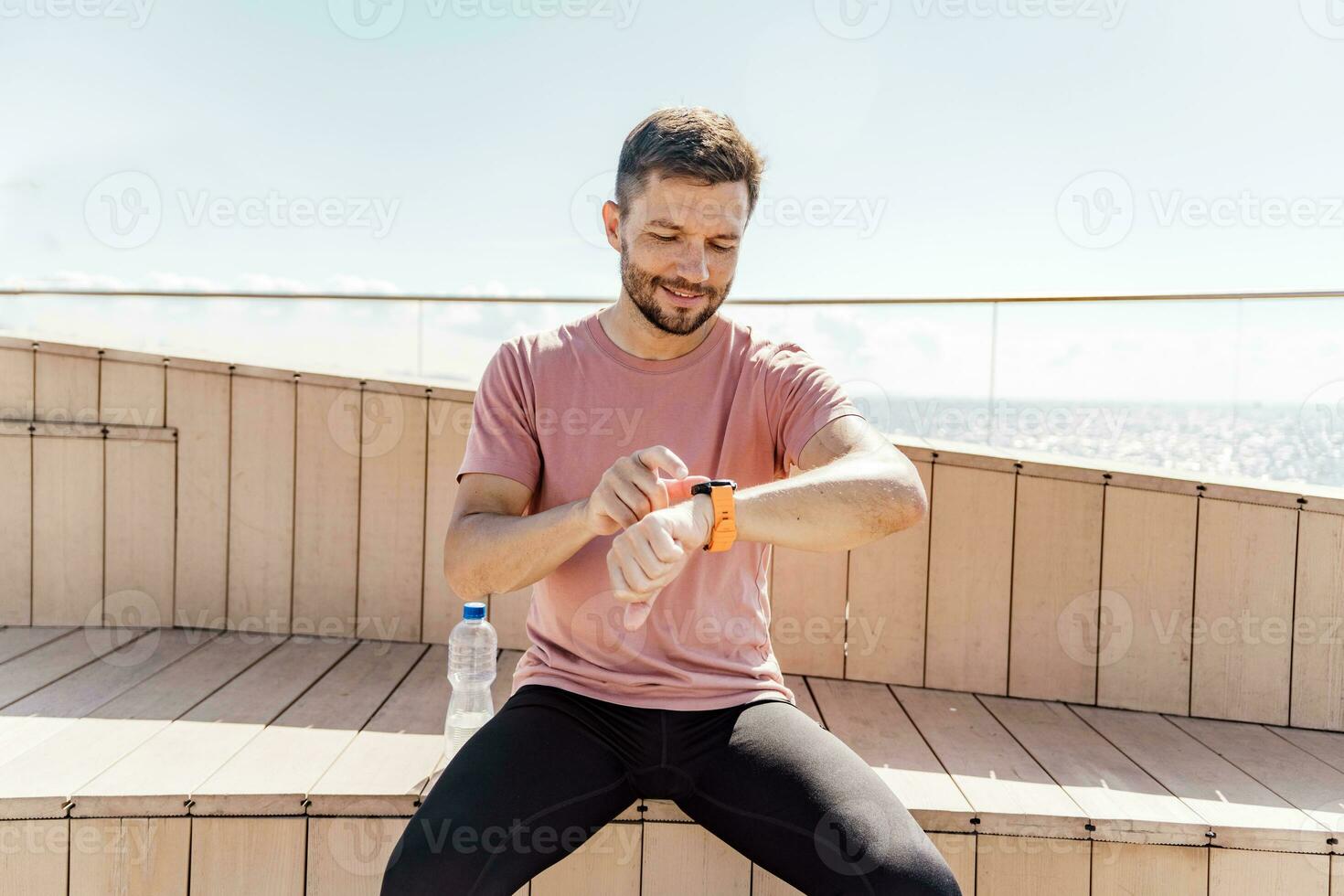 Looks at the screen on the fitness watch and the app. Athlete runner strong workout in sportswear. A sporty man running a lot. Man running in the city fresh air. photo