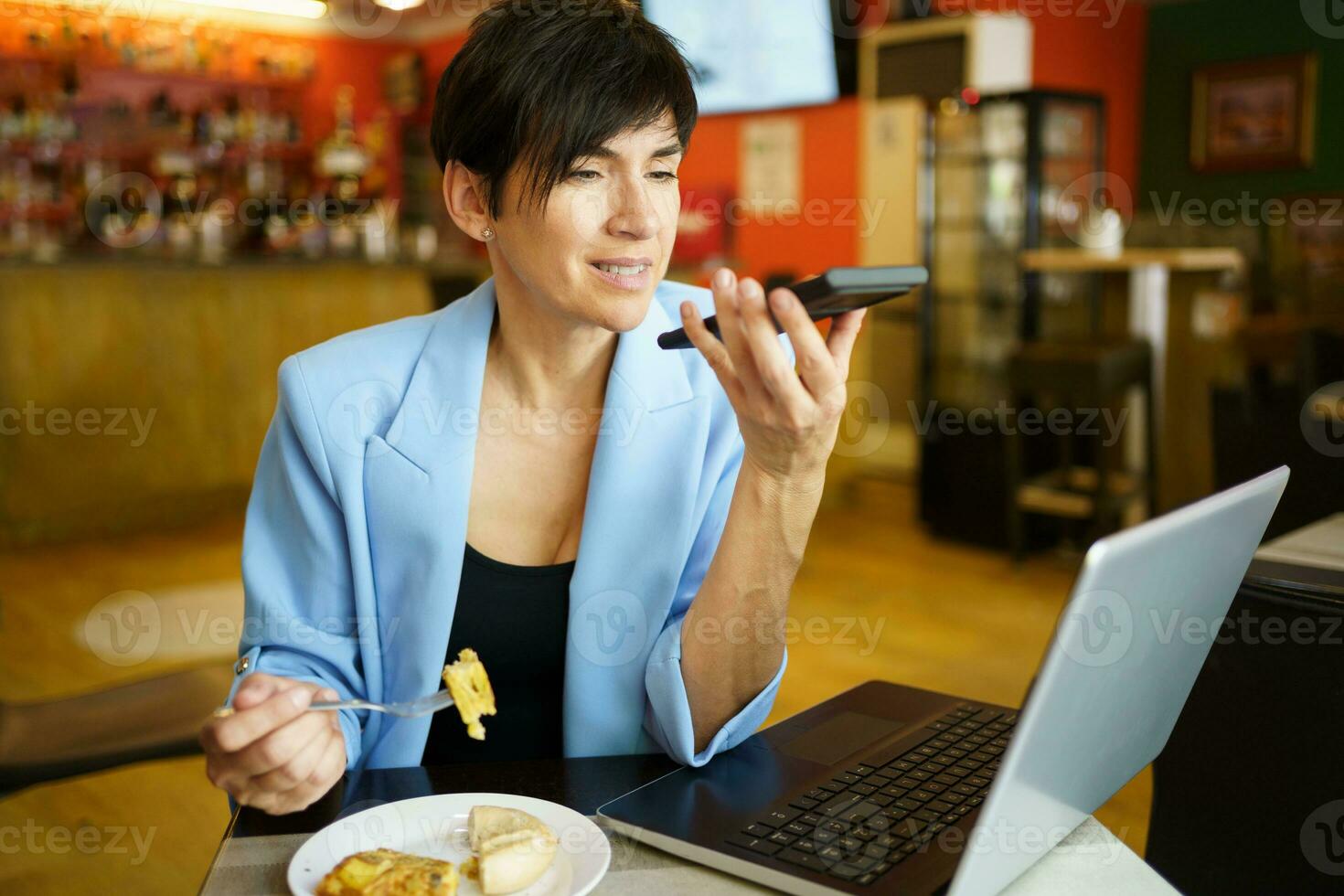 Serious woman recording audio message on smartphone while eating in cafe photo