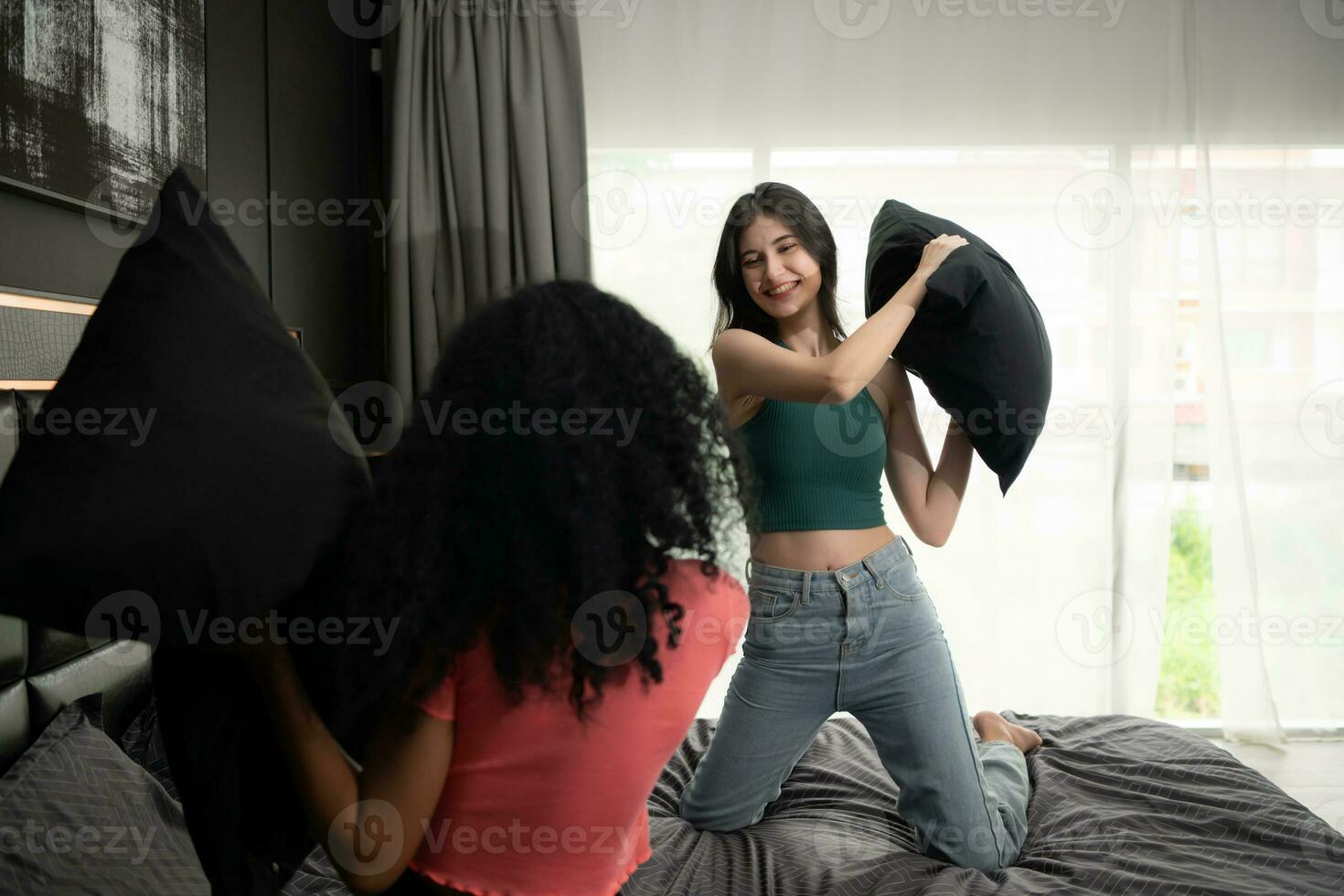 dos joven mujer jugar con almohadas en el cama en el dormitorio a hogar. amistad y estilo de vida concepto. foto