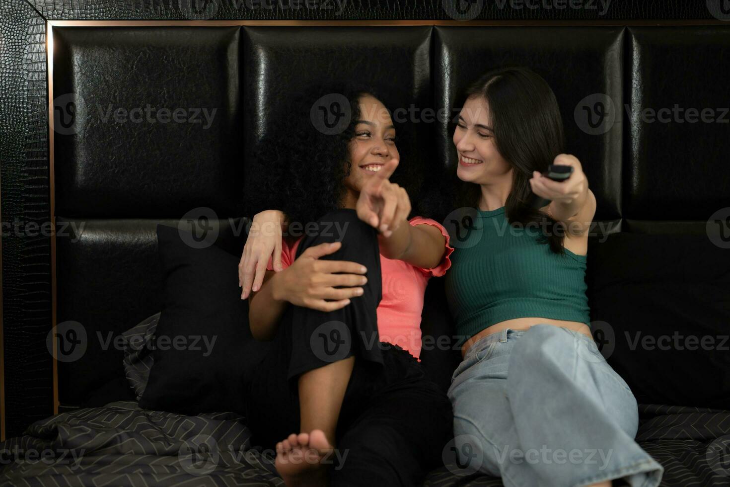 Two young women sitting on a bed and watching TV in a hotel room photo