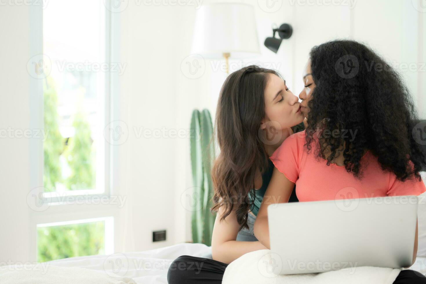 contento lesbiana Pareja utilizando ordenador portátil en cama a hogar. joven multiétnico lesbiana Pareja utilizando ordenador portátil juntos en dormitorio. tecnología y amor concepto foto