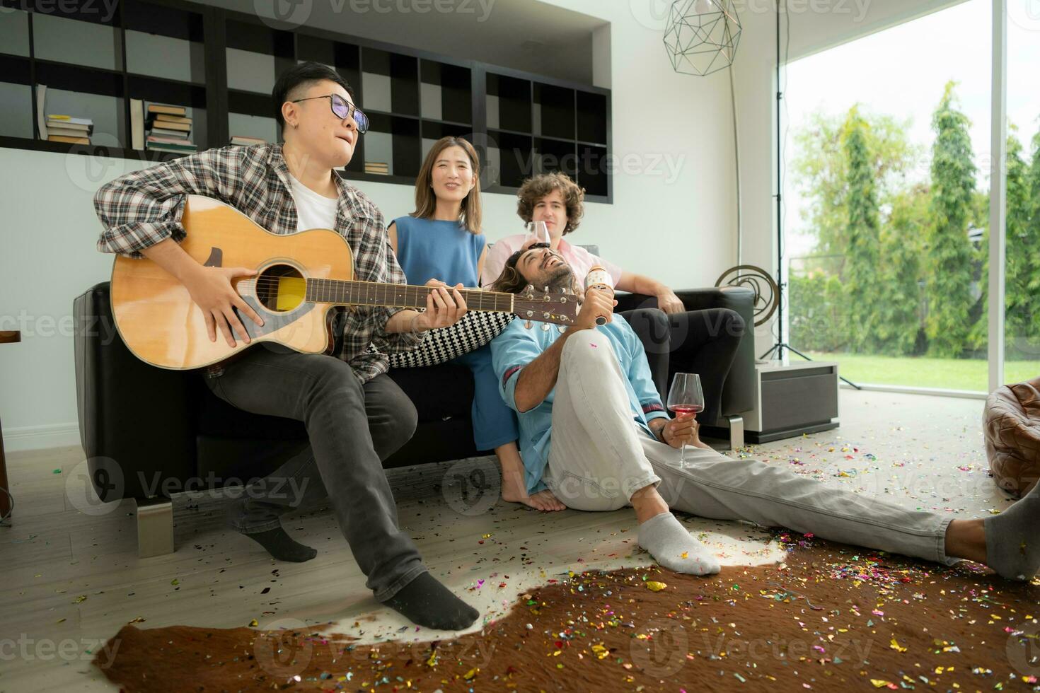 multiétnico grupo de amigos teniendo divertido jugando guitarra y canto juntos a hogar foto