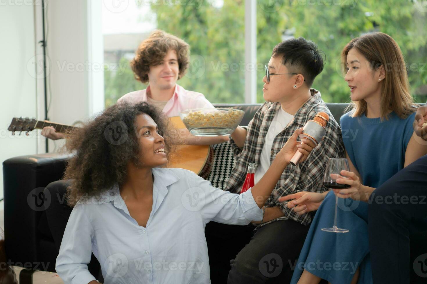 grupo de multiétnico amigos teniendo divertido a fiesta por jugando guitarra y canto juntos a hogar. foto