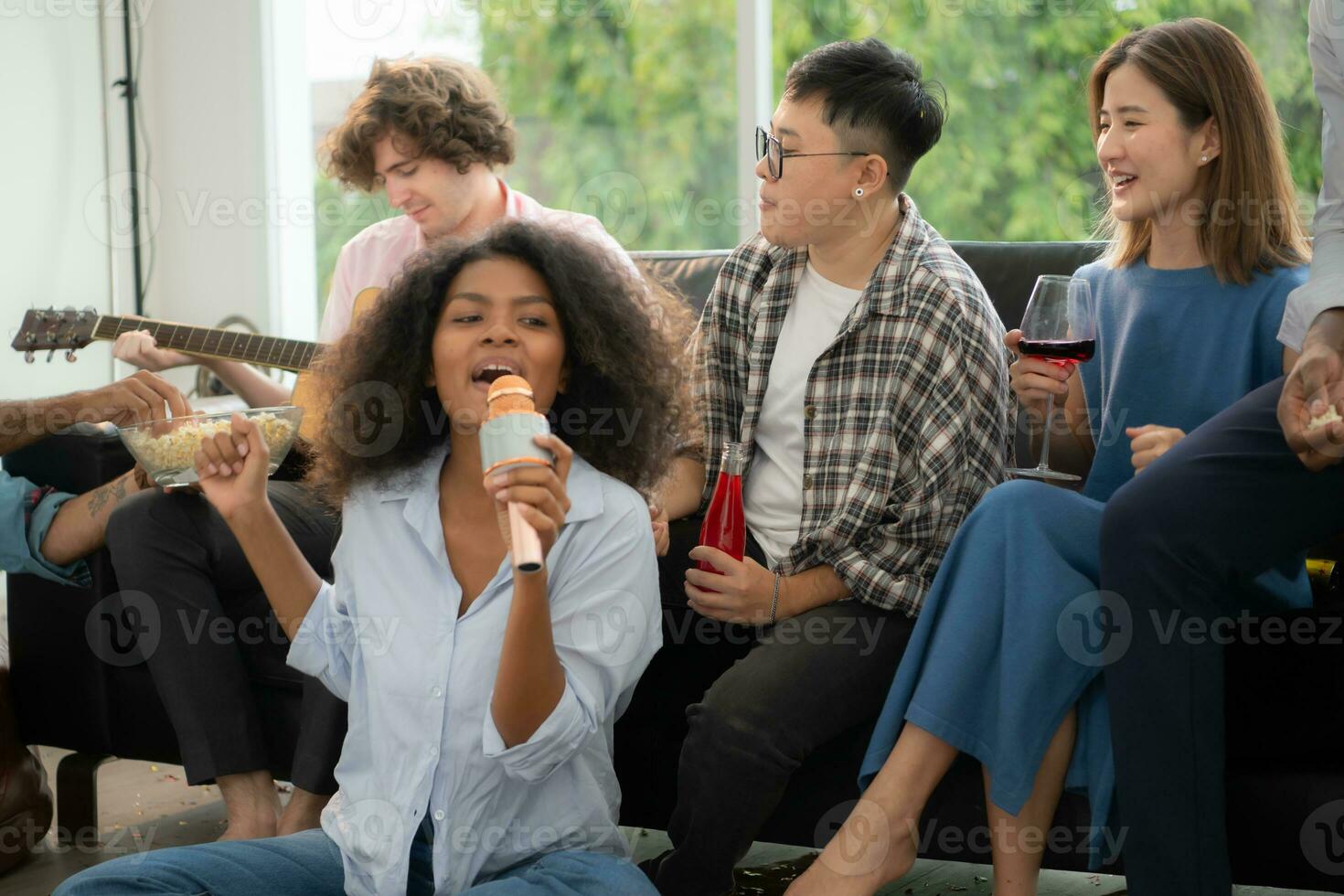 Group of multiethnic friends having fun at party by playing guitar and singing together at home. photo