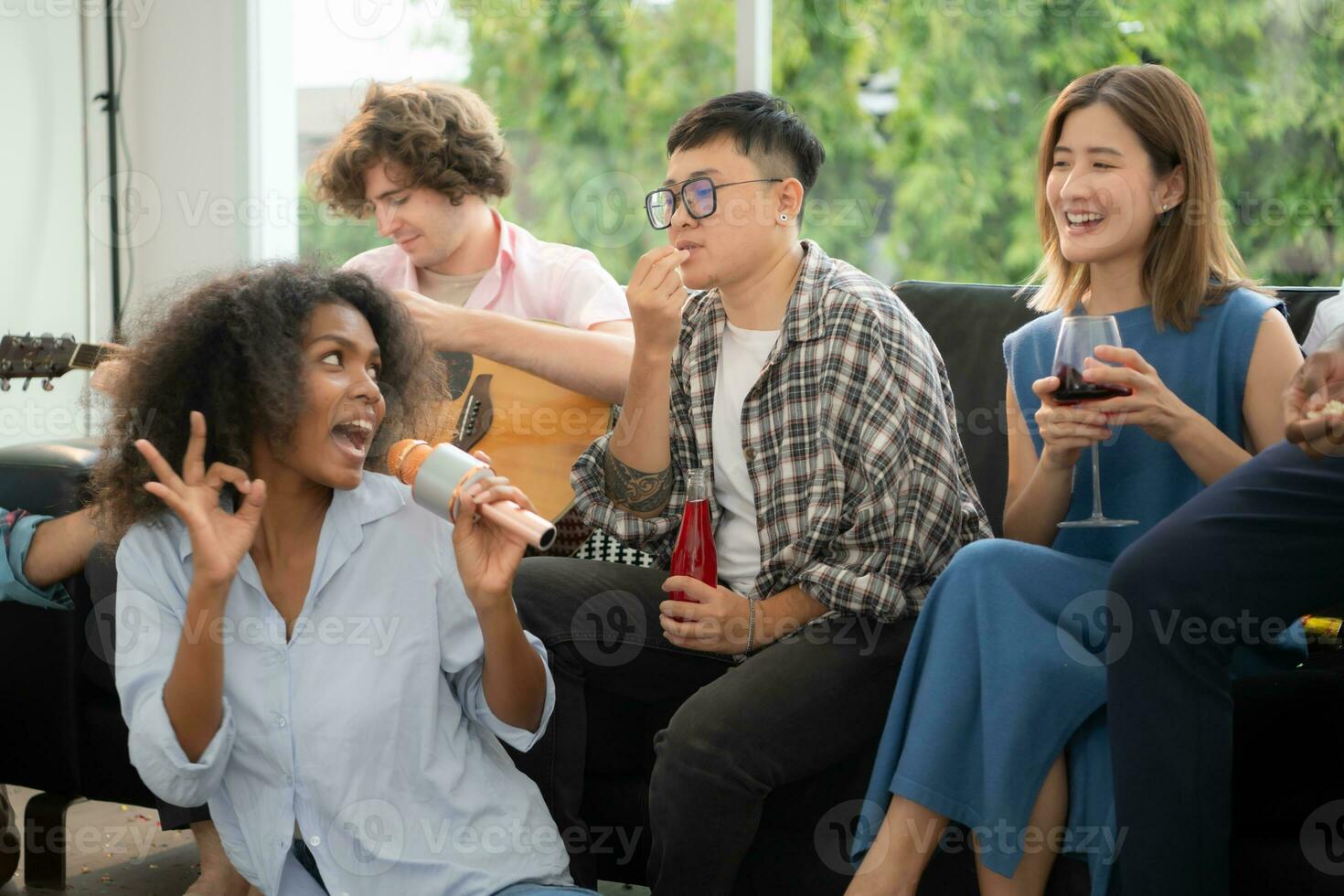 Group of multiethnic friends having fun at party by playing guitar and singing together at home. photo