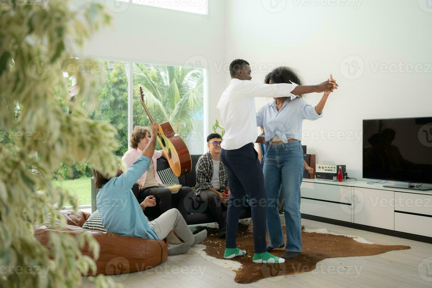 grupo de multiétnico amigos teniendo divertido a fiesta por jugando guitarra, canto y danza juntos a hogar. foto