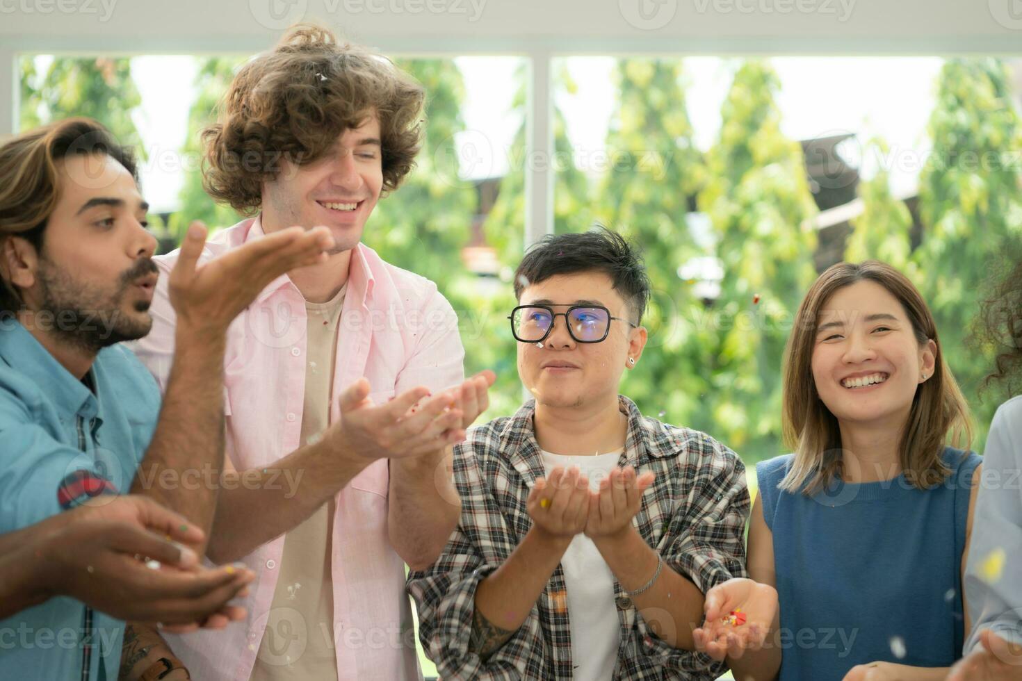 Group of multiethnic friends having fun at party playing fun blowing colorful paper photo