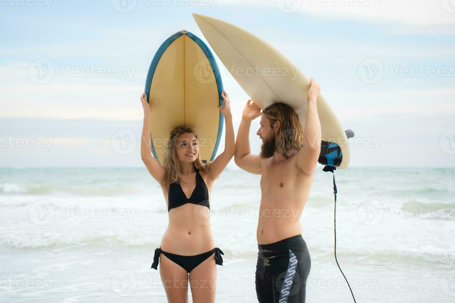 Young man and woman holding surfboards on their heads and walk into the sea to surf photo