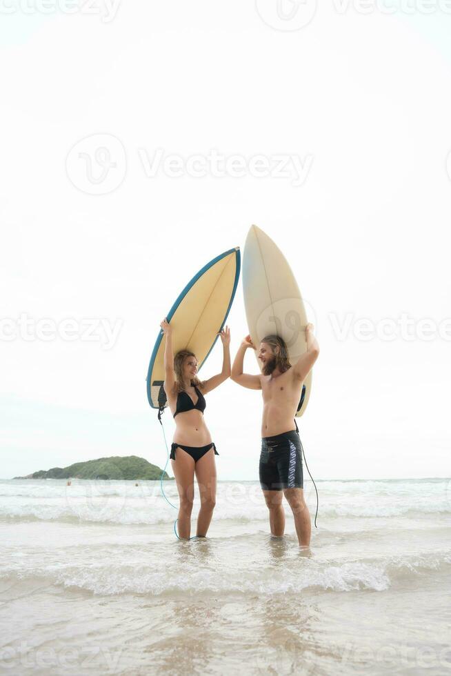 joven hombre y mujer participación tablas de surf en su cabezas y caminar dentro el mar a navegar foto