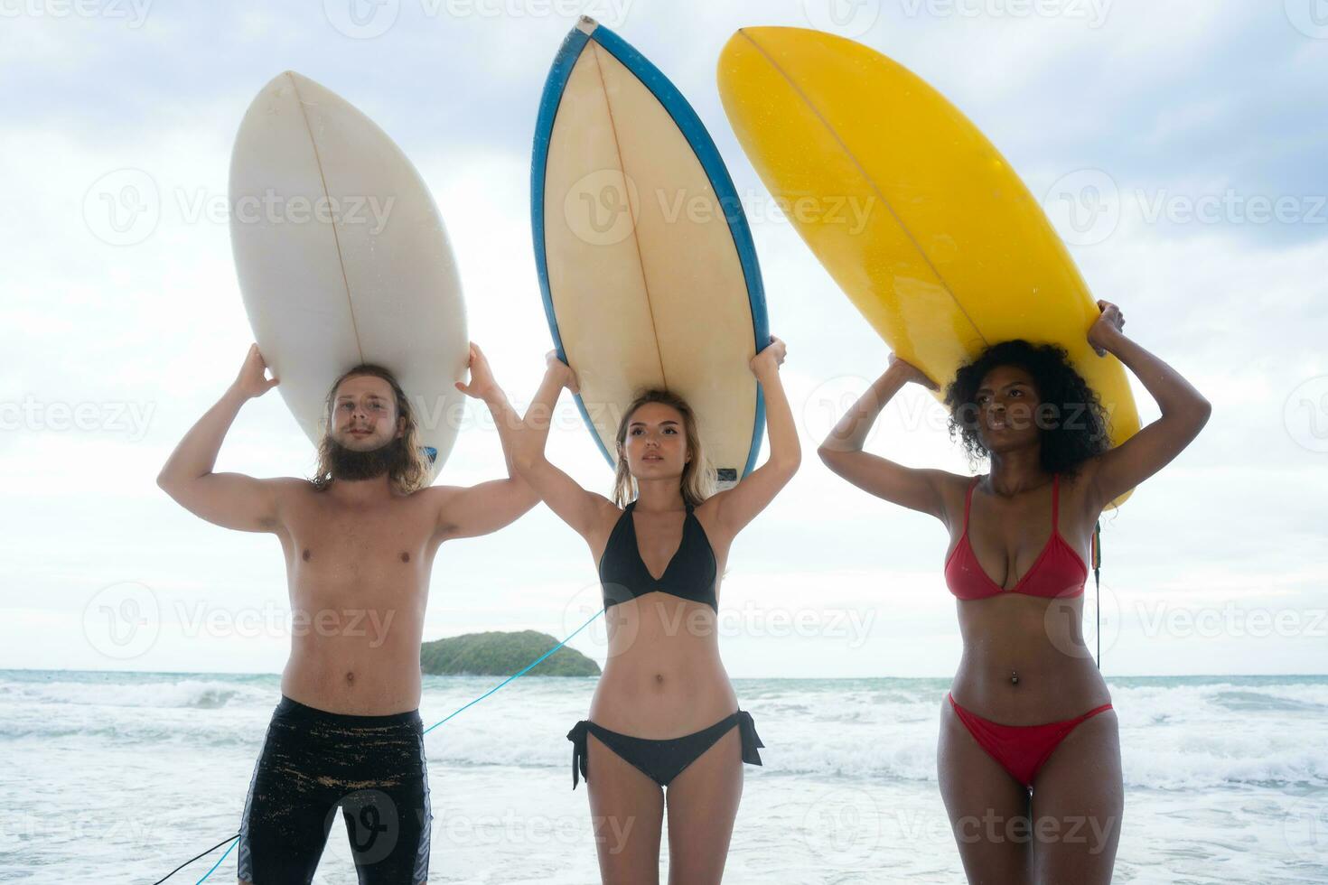 Rear view of two women and young man holding surfboards on their heads and walk into the sea to surf photo