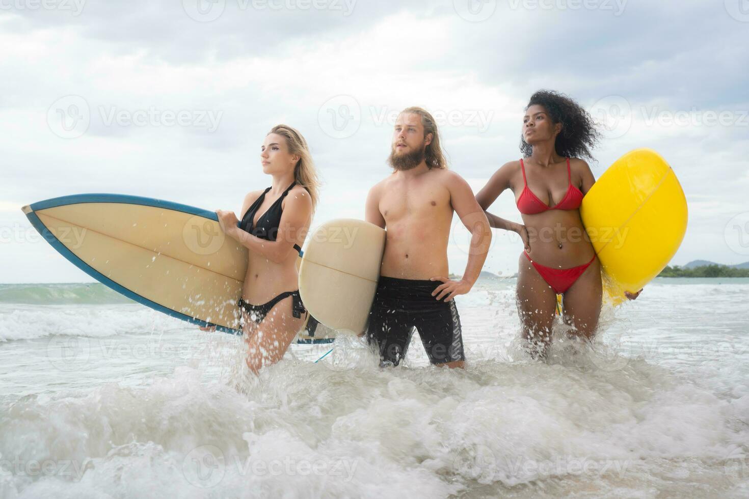 Two women and young man holding surfboards ready to walk into the sea to surf. photo