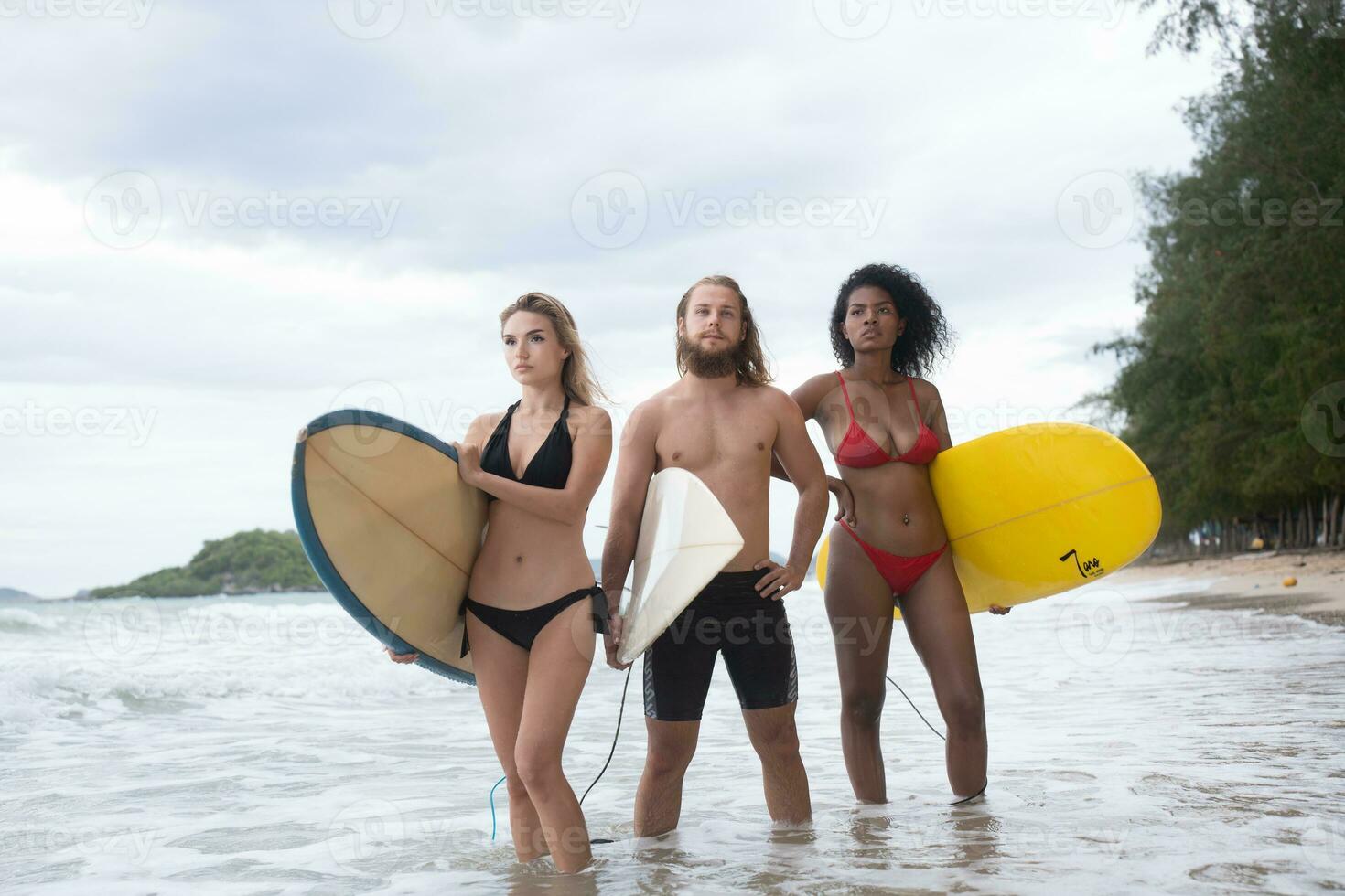 Two women and young man holding surfboards ready to walk into the sea to surf. photo