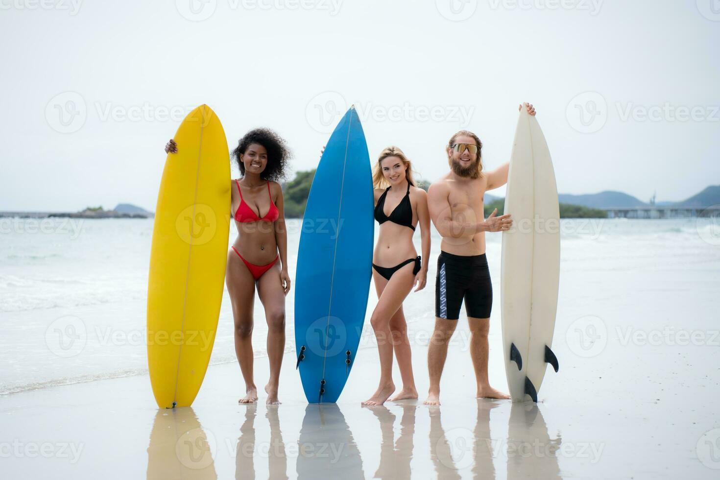 Group of friends in swimsuits posing with surfboards on the beach. photo