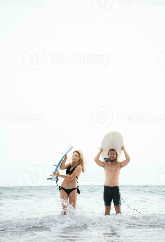 Young man and woman holding surfboards on their heads and walk into the sea to surf photo