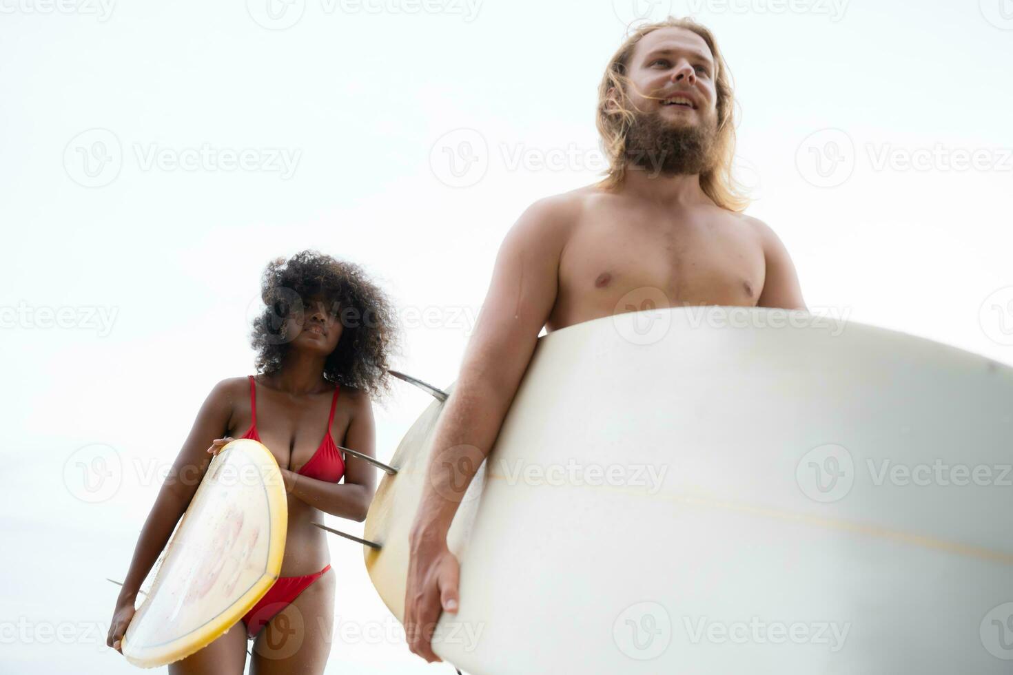 Young men teaching surfing with a surfboard with young women in red swimsuits photo