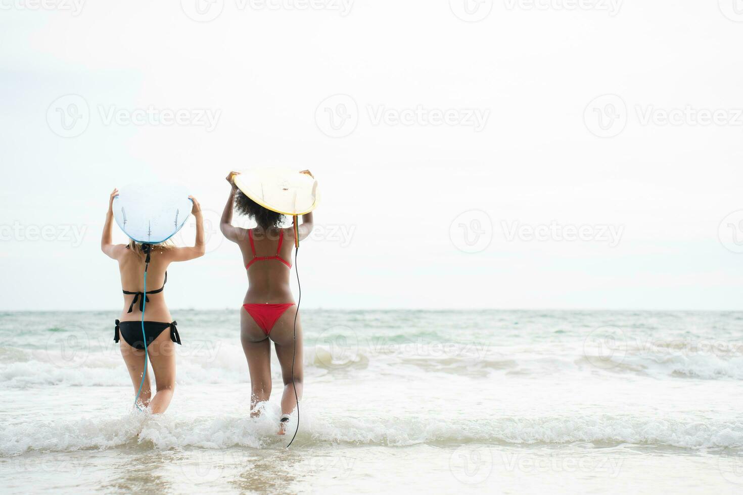 Rear view of two women and young man holding surfboards on their heads and walk into the sea to surf photo