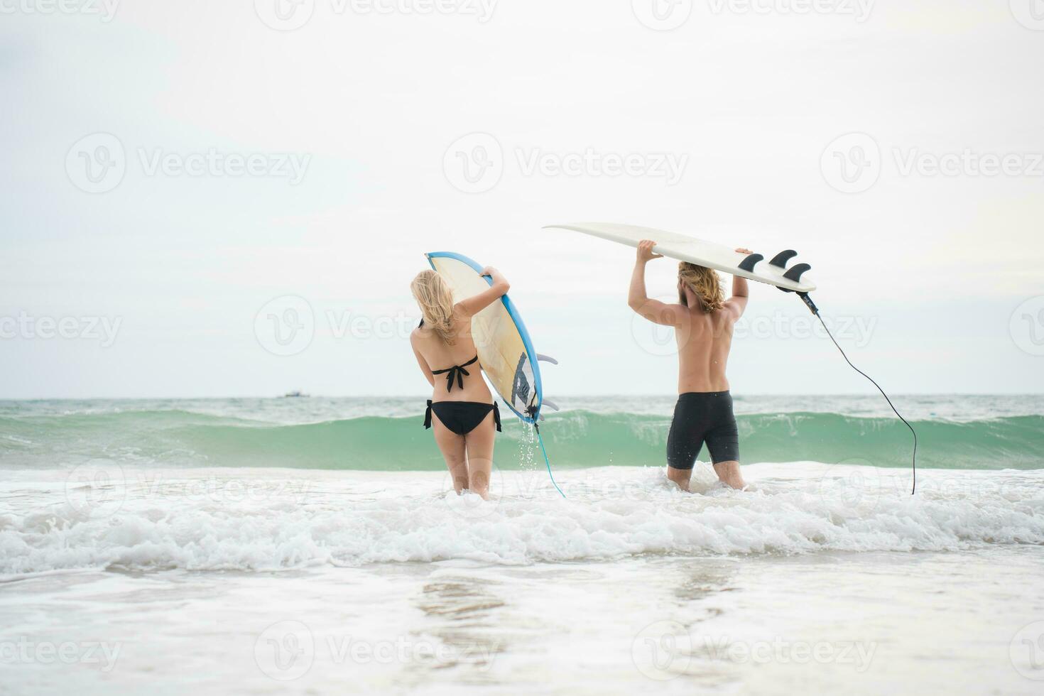 Young man and woman holding surfboards on their heads and walk into the sea to surf photo