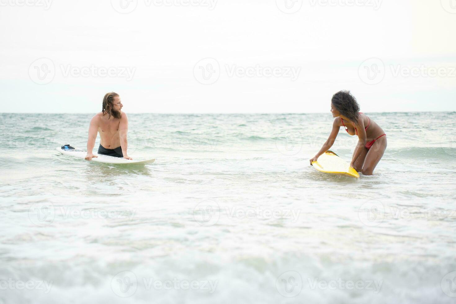 Young men teaching surfing with a surfboard with young women in red swimsuits photo