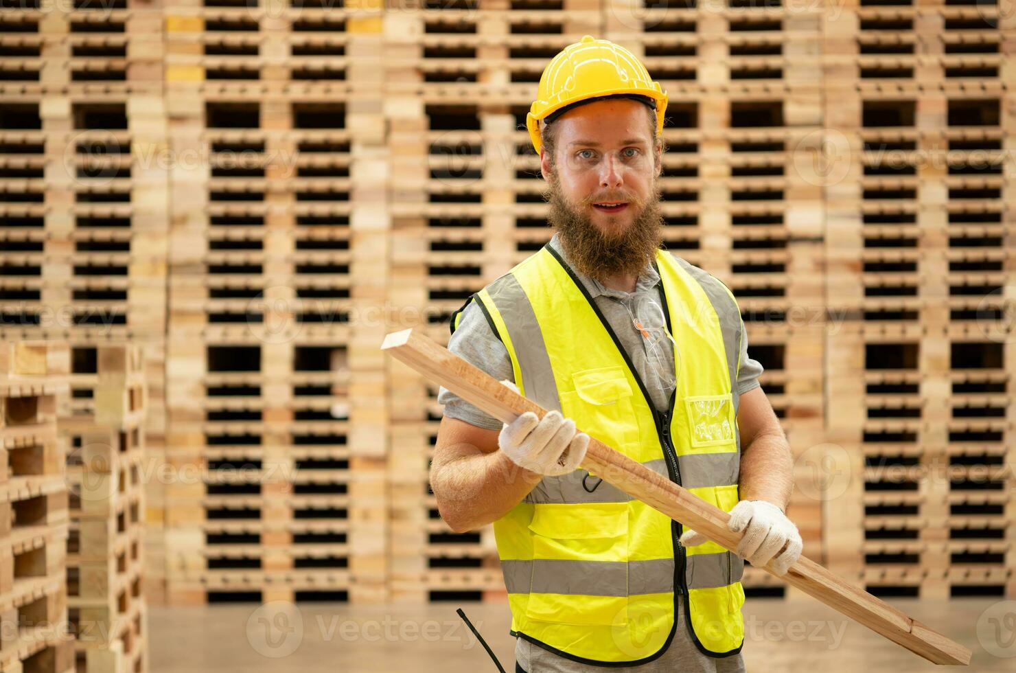 Portrait of young male carpenter working in a woodworking factory, He is wearing a safety helmet and glasses, Checking the wooden planks coming out of the wood grinder. photo