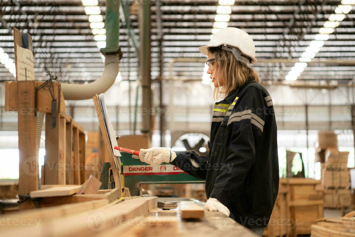 Female carpenter working in a woodworking factory, She is wearing a safety helmet and glasses. Checking the neatness of the planks against the design documents. photo