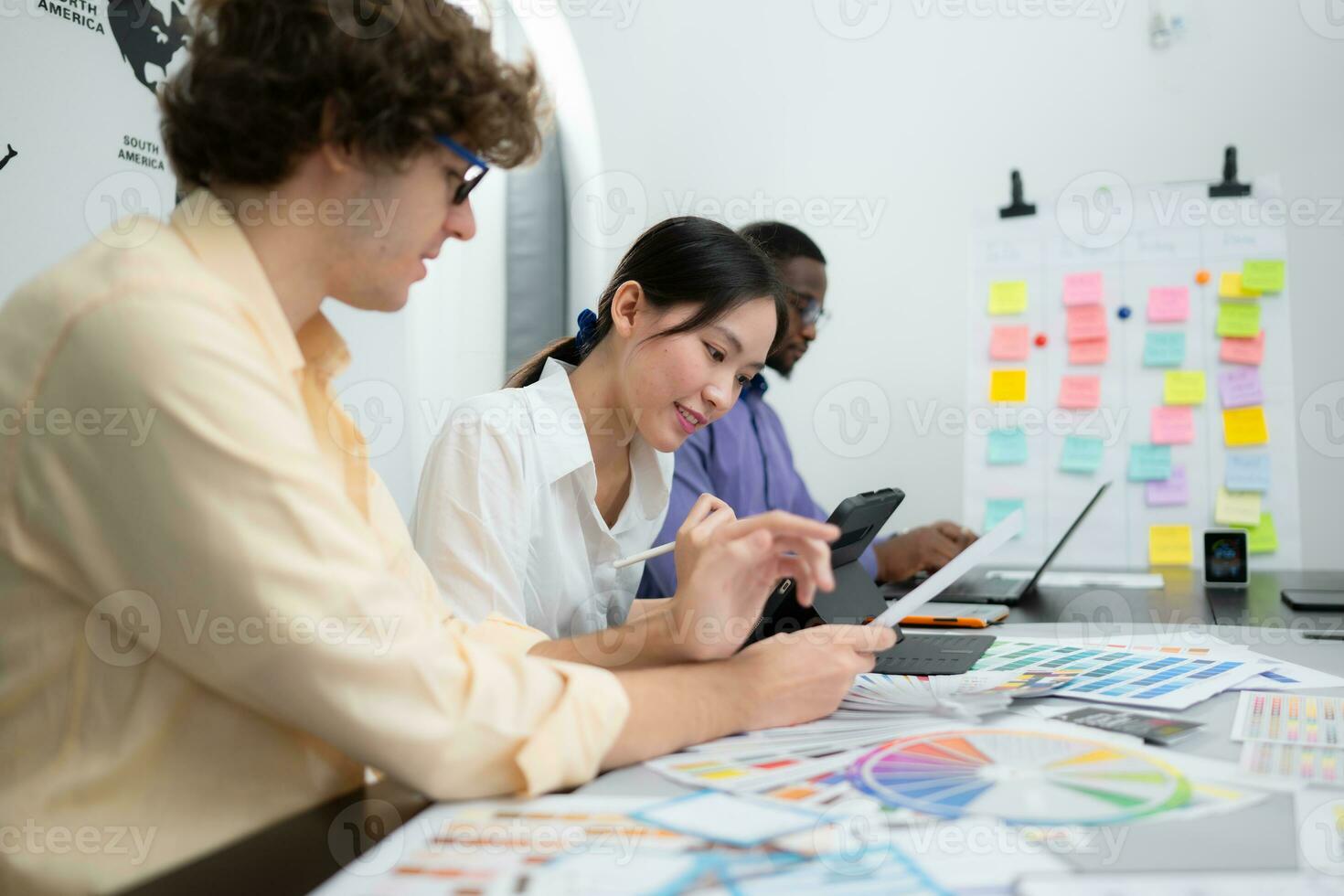 Multiethnic team of architects and designers are meeting to brainstorm design an application smartphone on a bright modern office working on a laptop. photo