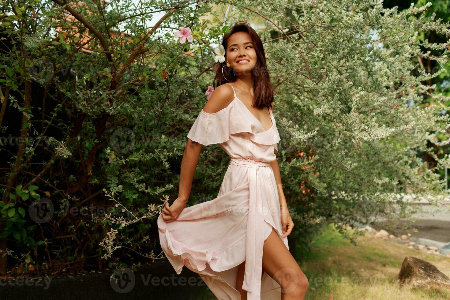 Graceful Asian woman with perfect skin  and hibiscus flower in hairs posing over wood wall and tropical plants. Summer fashion portrait. photo