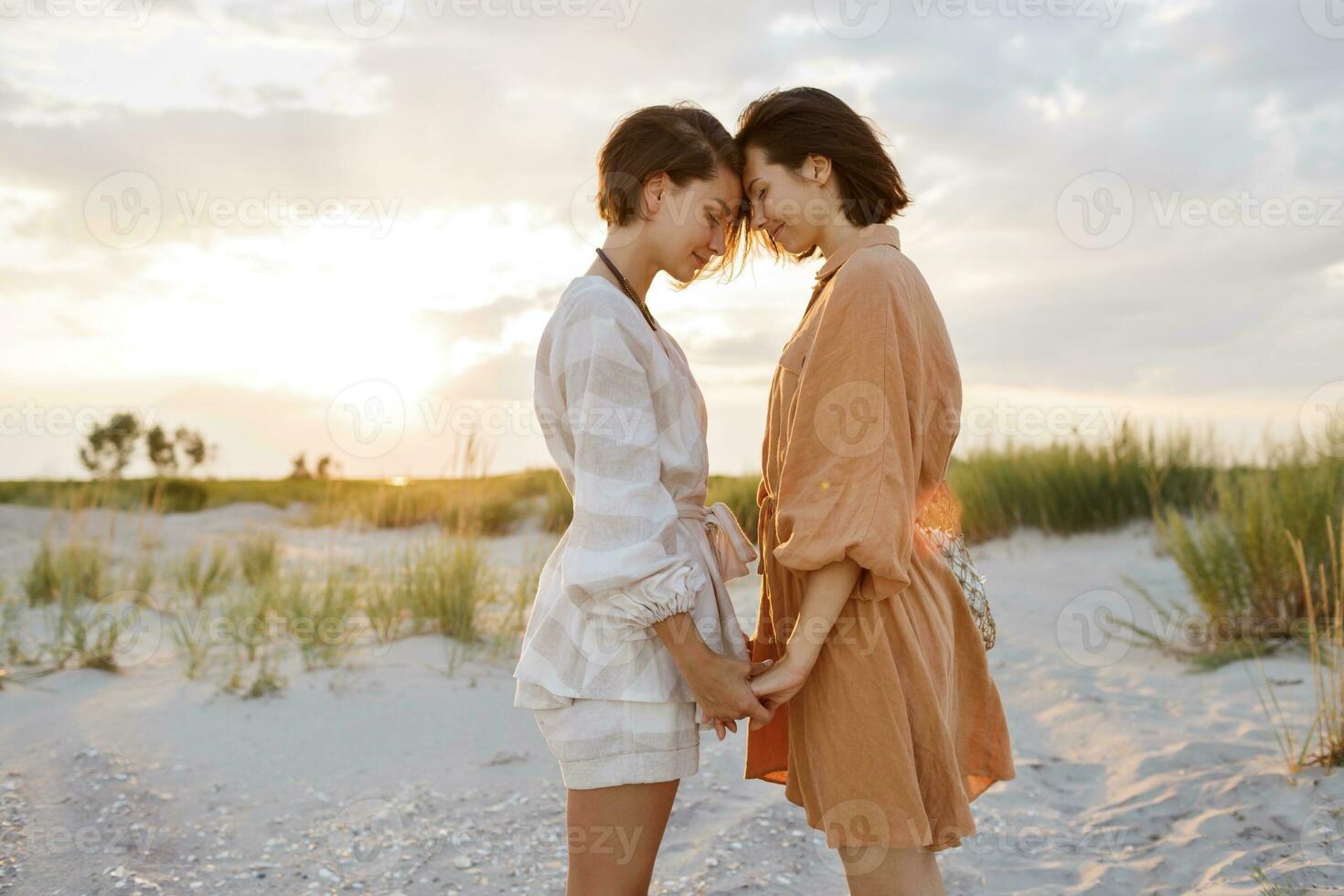 Summer fashion image of two  brunette european women in linen clothes posing on the beach photo