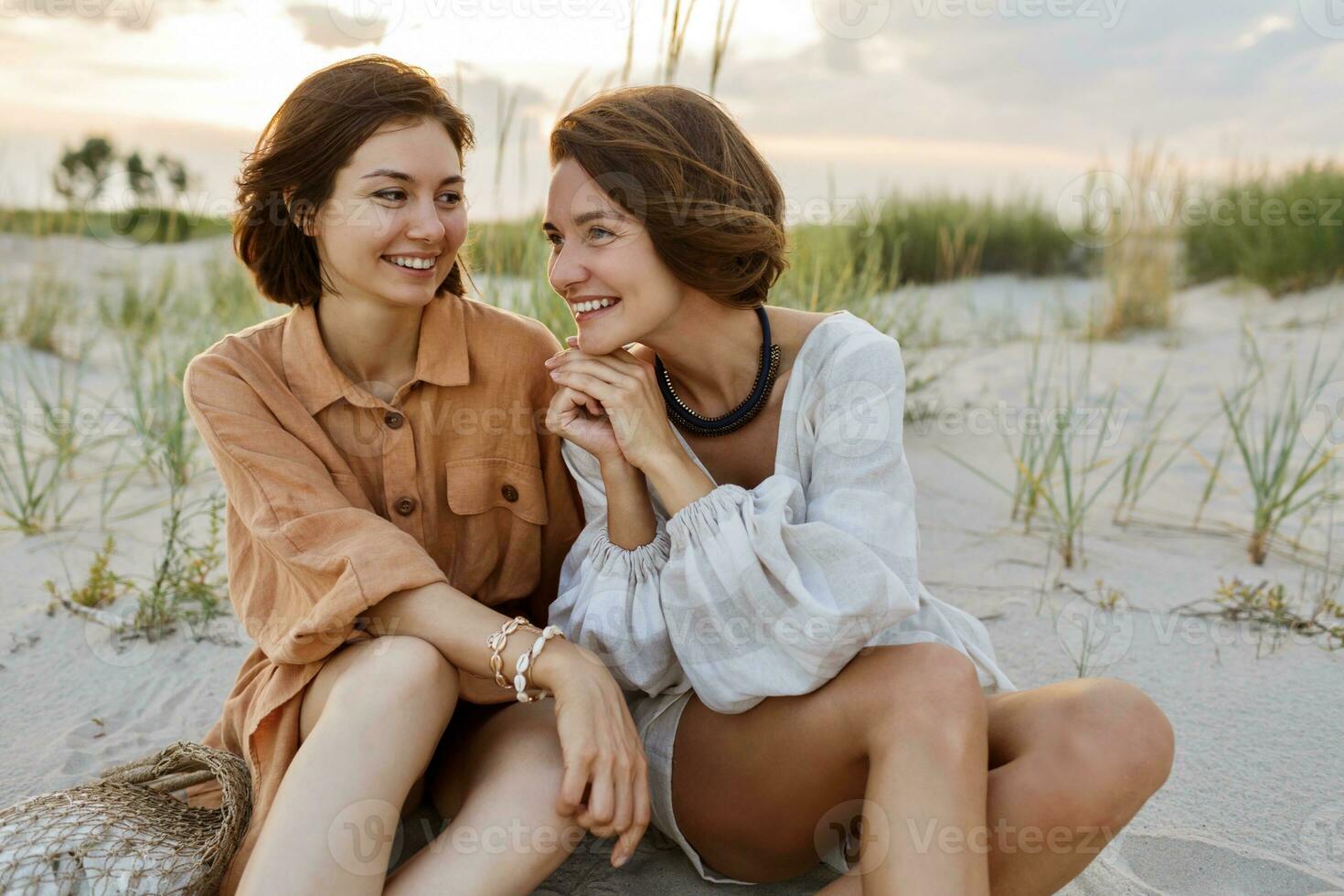 Summer fashion image of two  brunette european women in linen clothes posing on the beach photo