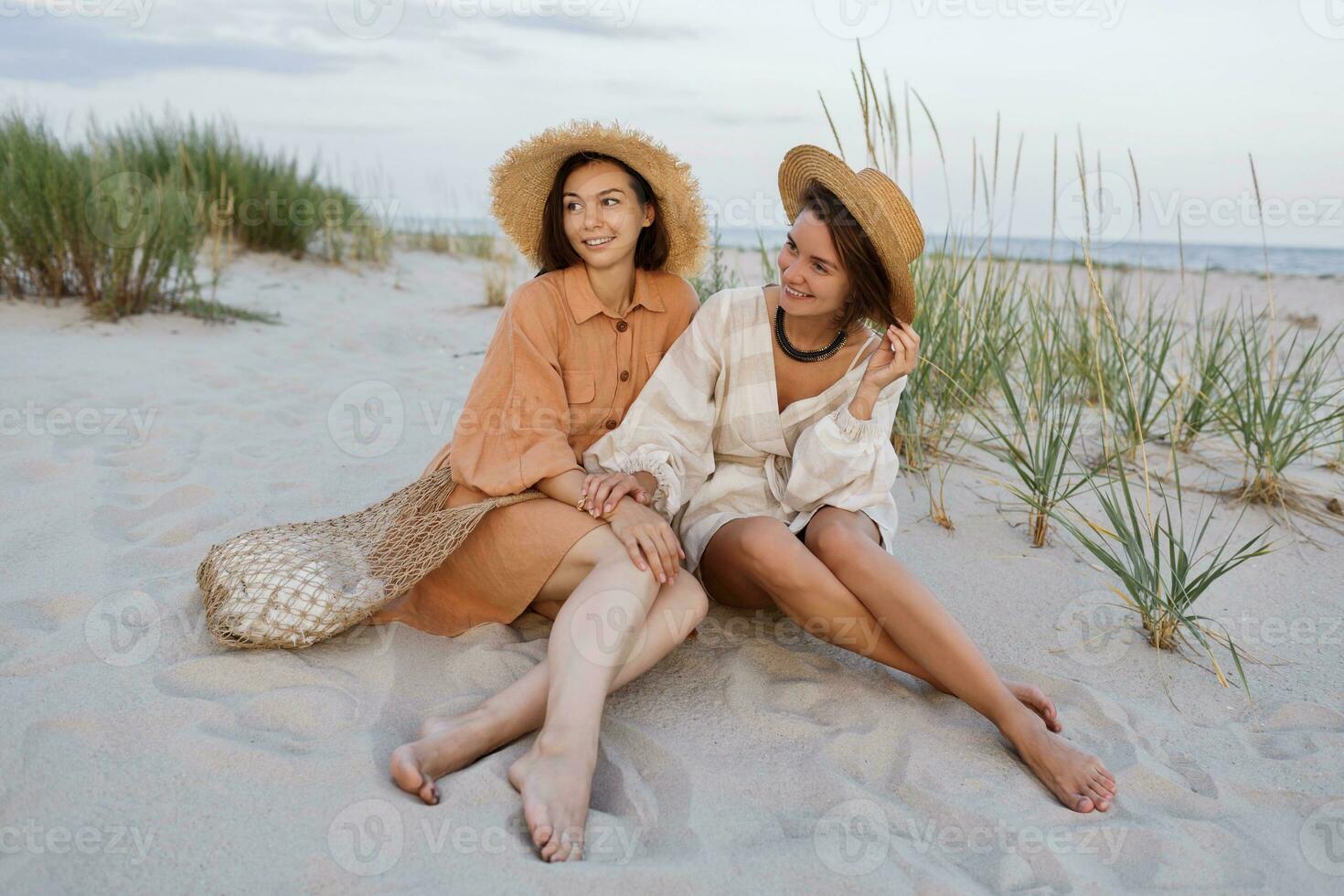 Summer fashion image of two  brunette european women in linen clothes posing on the beach photo