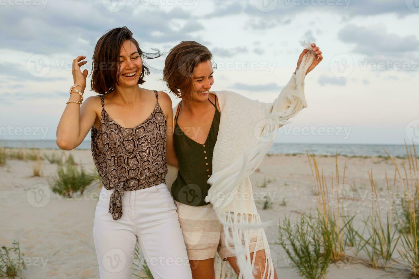 Summer fashion image of two  brunette european women in linen clothes posing on the beach photo