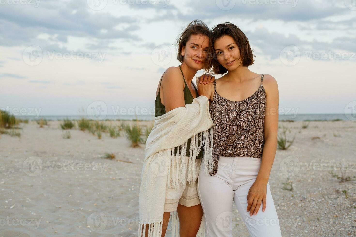 Summer fashion image of two  brunette european women in linen clothes posing on the beach photo
