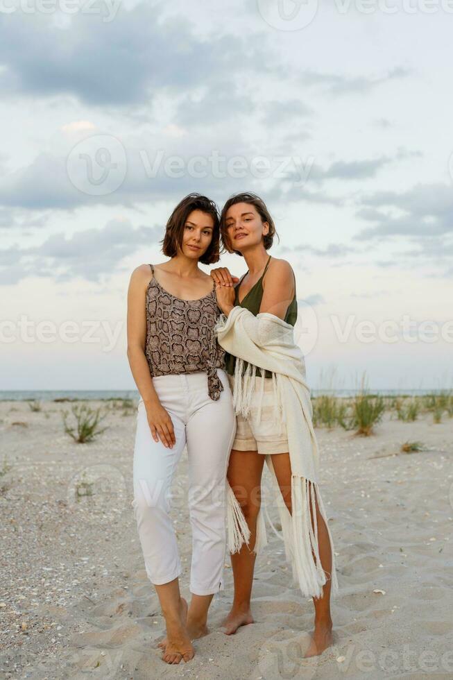 Summer fashion image of two  brunette european women in linen clothes posing on the beach photo