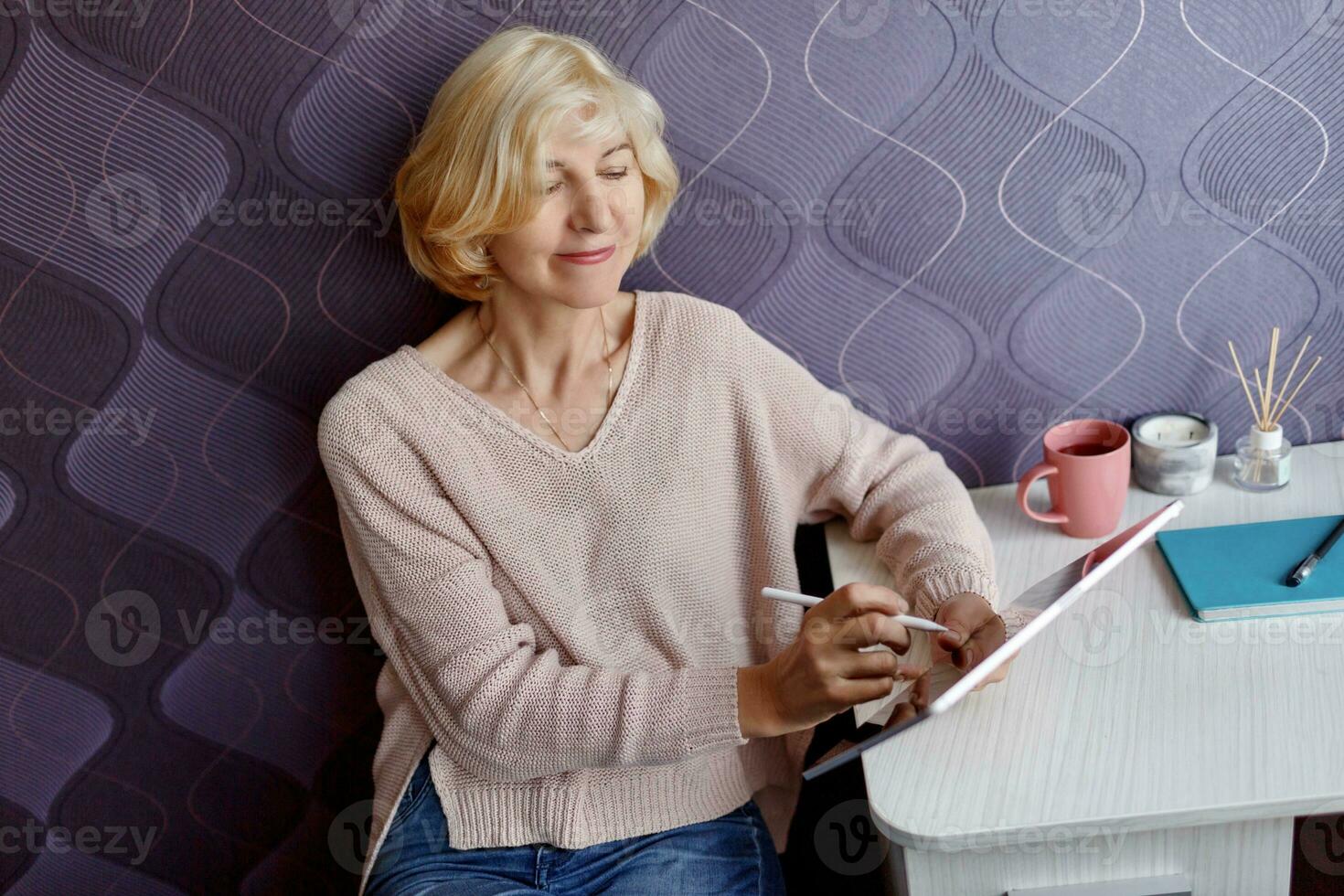 Smiling mature woman using mobile phone while working by computer at home. photo